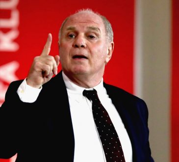 Uli Hoeneß im Anzug vor einer roten Pressewand