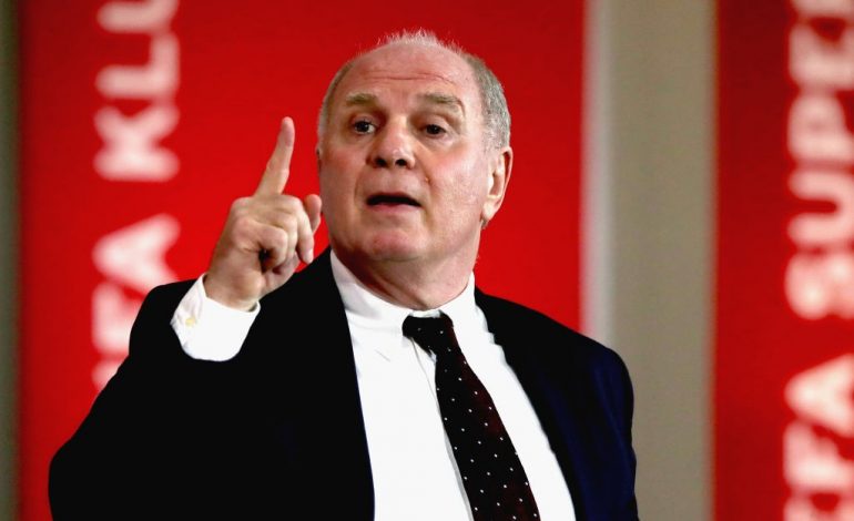 Uli Hoeneß im Anzug vor einer roten Pressewand