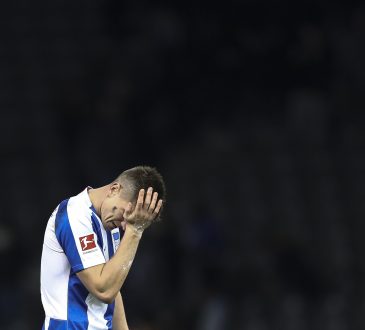 Ein Hertha Spieler fasst sich ins Gesicht, der Hintergrund erscheint schwarz.