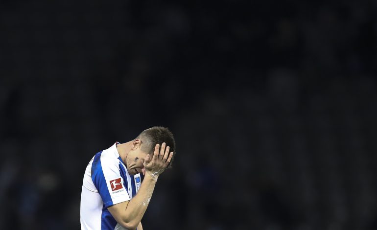 Ein Hertha Spieler fasst sich ins Gesicht, der Hintergrund erscheint schwarz.