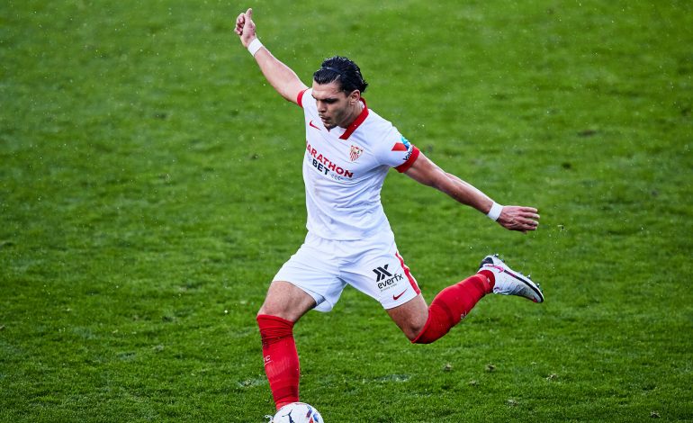 Ein schwarzhaariger Fussballspieler im weißen Trikot schießt einen Ball