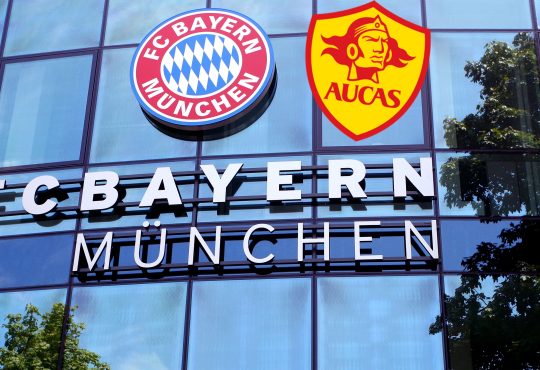 Die FC Bayern Geschäftsstelle mit dem Logo des FCB und dem Logo von SD Aucas