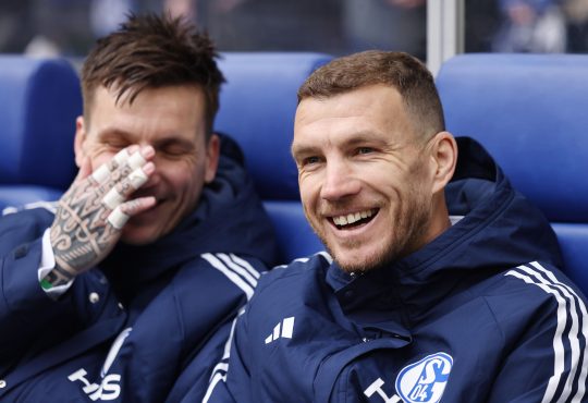Edin Dzeko in einer Schalke 04 Trainingsjacke auf der Auswechselbank.