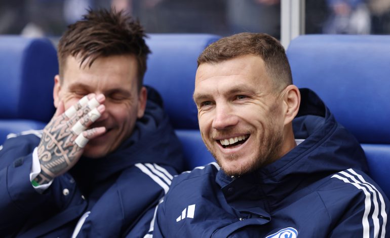 Edin Dzeko in einer Schalke 04 Trainingsjacke auf der Auswechselbank.