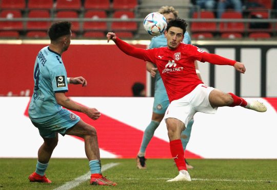 Timur Gayret nimmt einen Ball vor einem Verteidiger Volley.