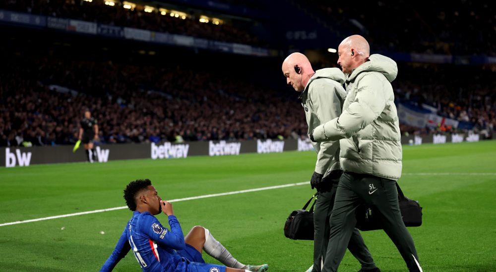 Estevao von Chelsea sitzt verletzt am Boden, zwei Betreuer gehen zu ihm.