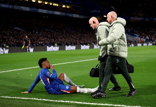 Estevao von Chelsea sitzt verletzt am Boden, zwei Betreuer gehen zu ihm.