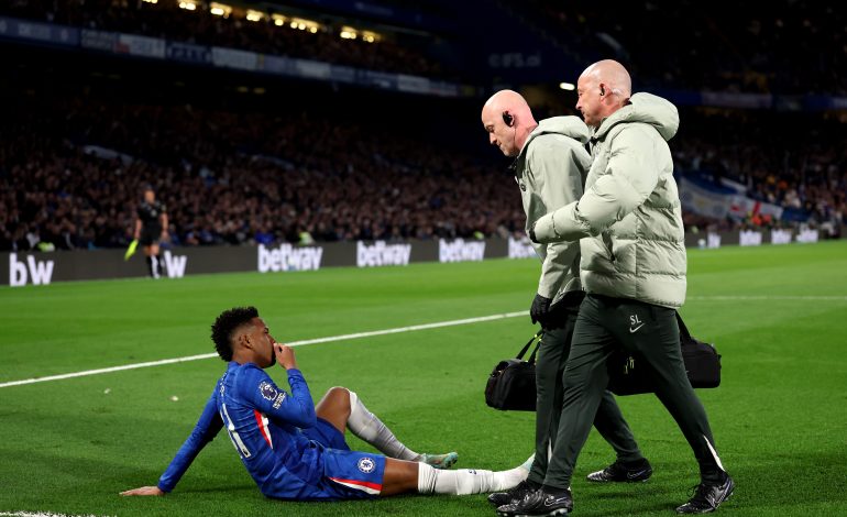 Estevao von Chelsea sitzt verletzt am Boden, zwei Betreuer gehen zu ihm.